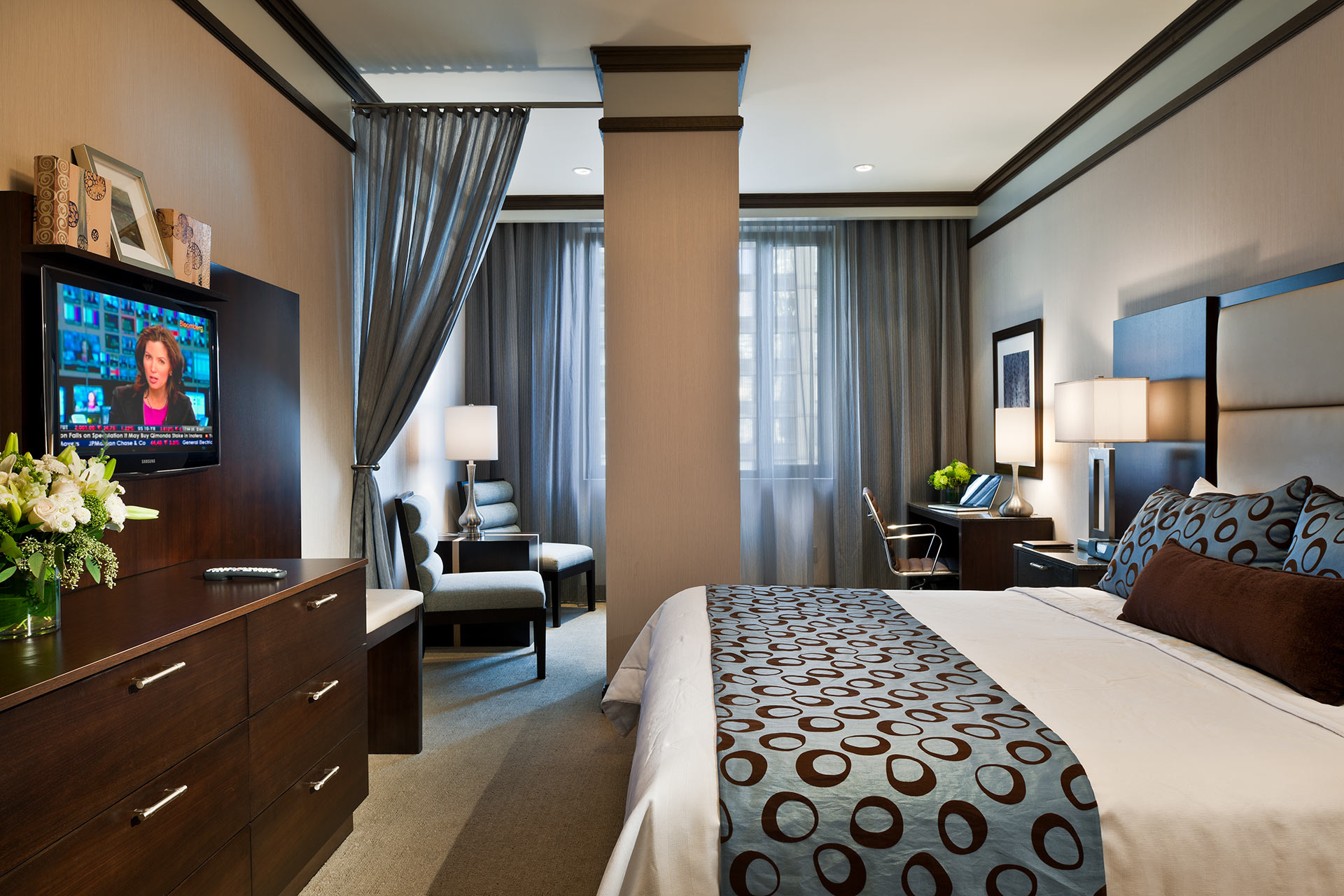 A wide view of a hotel room with a king-sized bed, desk, TV, and dresser.